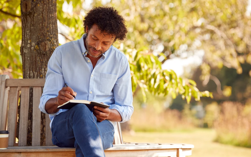 A person sitting on a bench writing in a journal